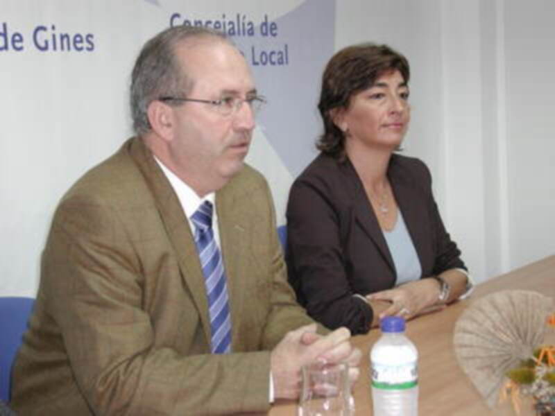 Dos personas sentadas en una mesa, uno con traje y corbata, la otra con chaqueta negra y blusa, en un contexto profesional o de negocios.