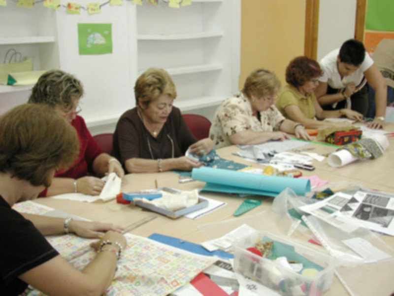 Grupos de personas participando en un taller de artesanía, trabajando con telas y otros materiales de costura.