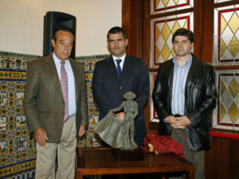 Tres hombres posan junto a una escultura en un entorno decorado con azulejos y vitrales.