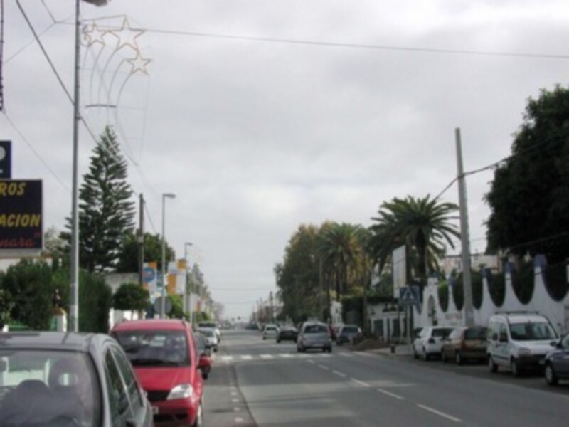 Vista de una calle urbana con coches en movimiento y decoración navideña en el borde de la carretera.