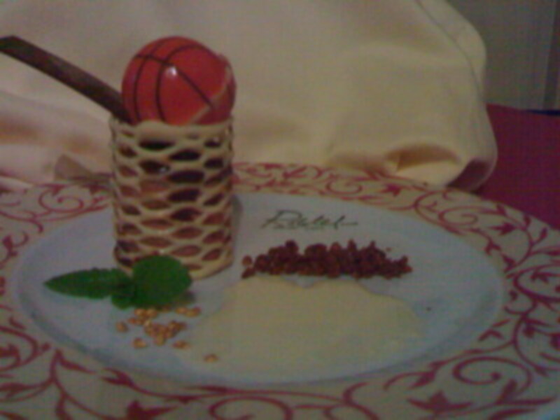 Un delicioso postre en forma de baloncesto con una cinta de azúcar y un palo de canela, acompañado de una hoja de menta fresca y un poco de granos de canela en el centro de la mesa.