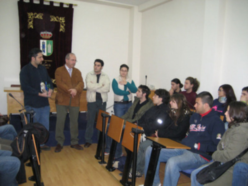 Reunión informativa en una sala de conferencias con participantes sentados y un presentador en el centro.
