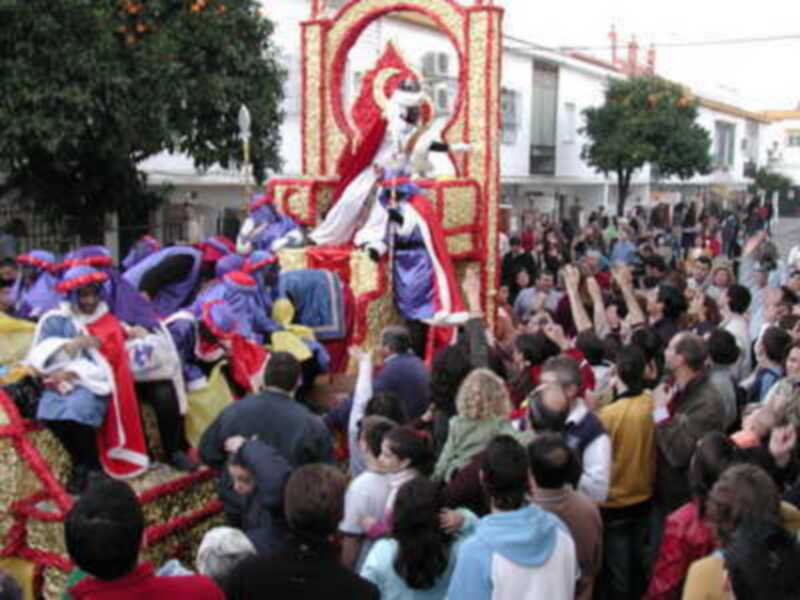 Fiesta de los Reyes Magos en una ciudad española, con un carro adornado y una multitud de personas disfrutando del evento.