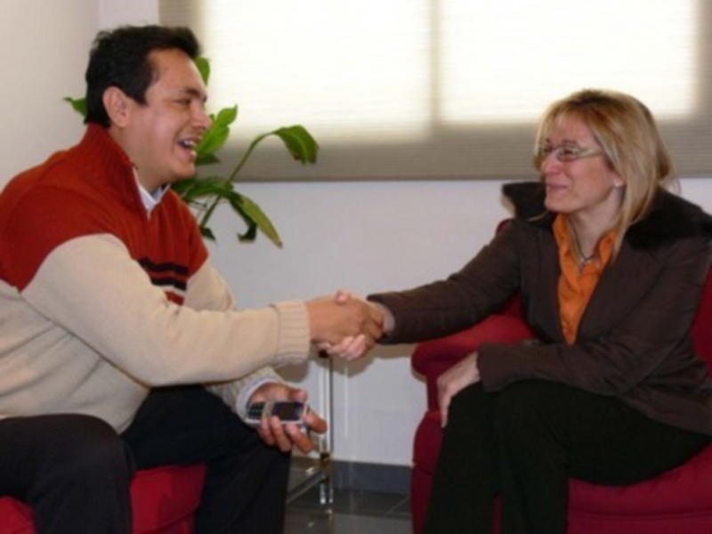 Dos personas sonrientes intercambiando un teléfono móvil en un entorno formal.