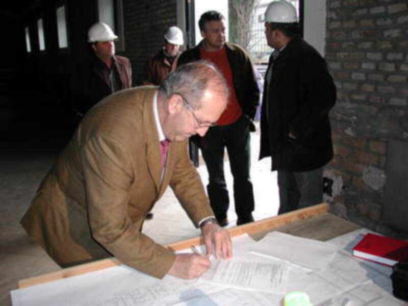 Un hombre revisa y firma documentos en un sitio de construcción mientras otros observan.