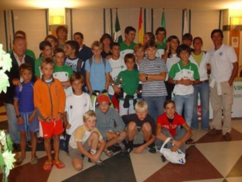 Equipo de jóvenes atletas posando para una foto en un salón con banderas de diferentes países en el fondo.