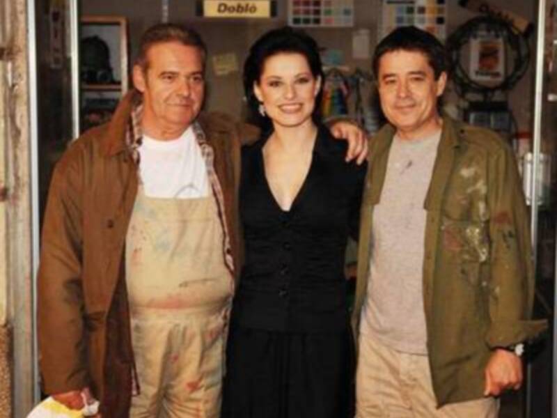 Tres personas sonrientes posando juntas en un espacio industrial, con estanterías de herramientas y materiales al fondo.