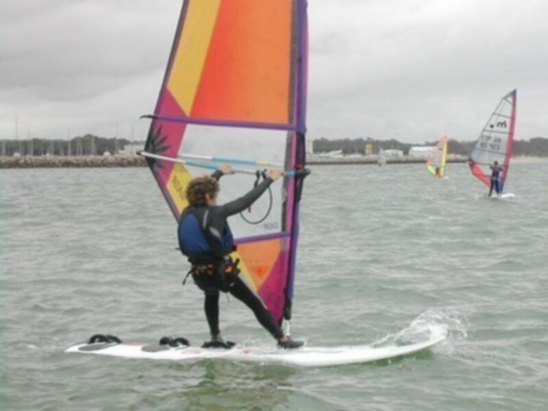 Práctica de windsurf en un día nublado con otros navegantes en el horizonte.