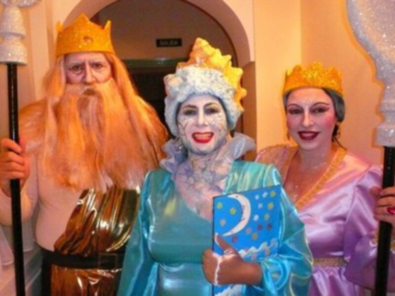 Personajes de teatro disfrazados con trajes y coronas, uno sosteniendo un escudo con un símbolo lunar.