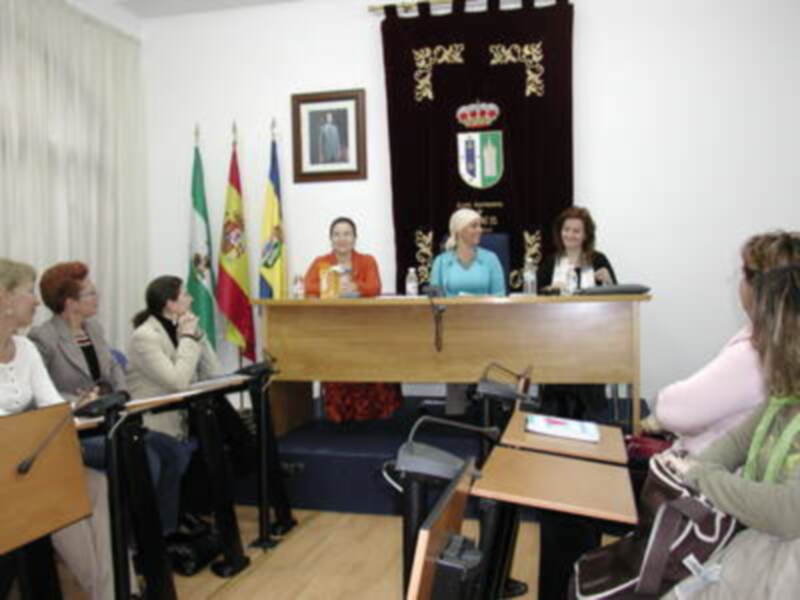 Una reunión formal con personas sentadas en mesas, hablando y tomando notas. En el fondo, se puede ver una bandera y un letrero con texto en español.