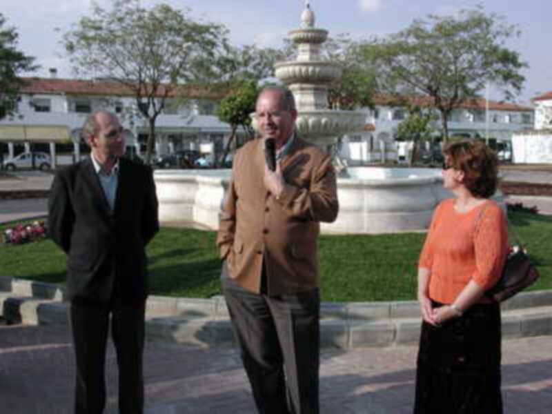 Tres personas conversando en un parque frente a una fuente monumental.