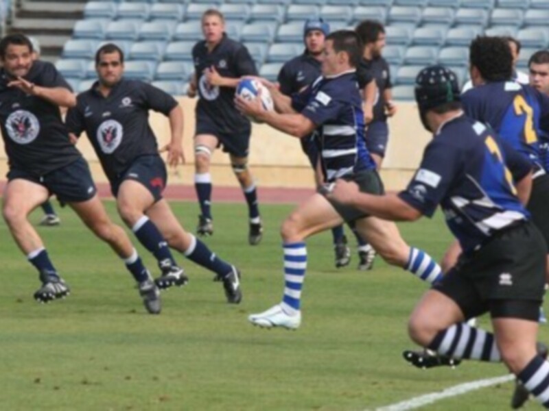 Un juego de rugby en un estadio con jugadores en acción y una pelota en el aire.