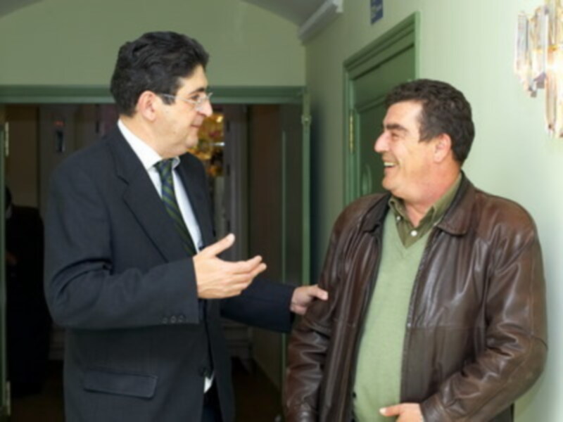 Dos hombres intercambian saludos en un pasillo de oficinas, expresando amistad y cordialidad.