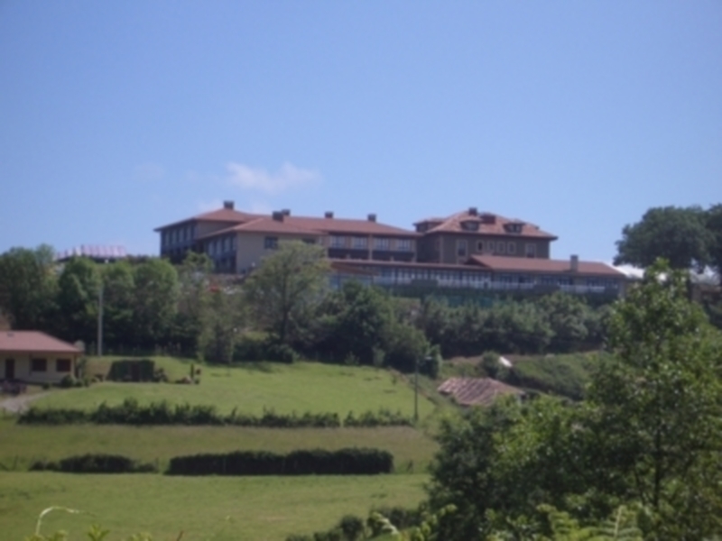 Elegante edificio residencial en una colina, rodeado de vegetación y un cielo azul claro.