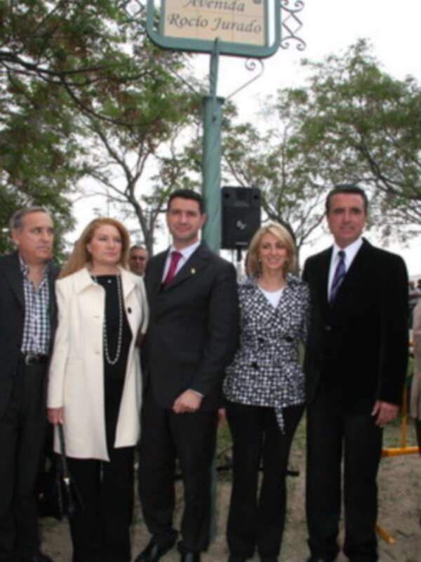 Fotografía de una familia en un evento formal, posando junto a una placa con el nombre de una avenida.