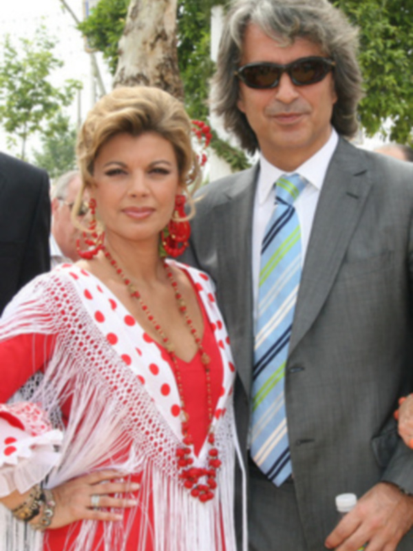 Una pareja elegante posa juntos en un evento formal, ella con un vestido rojo y blanco con flecos, él con traje y corbata.