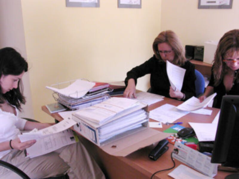 Trabajadoras en un escritorio lleno de documentos, concentradas en su tarea en un entorno de oficina.