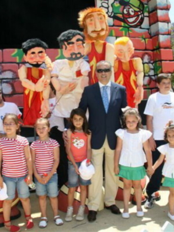 Un grupo de personas, incluyendo niños y adultos, posa frente a una escultura de personajes animados en un evento al aire libre soleado.