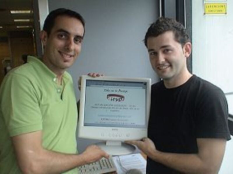 Dos hombres sonrientes sosteniendo una computadora portátil con un mensaje en hindi en la pantalla.