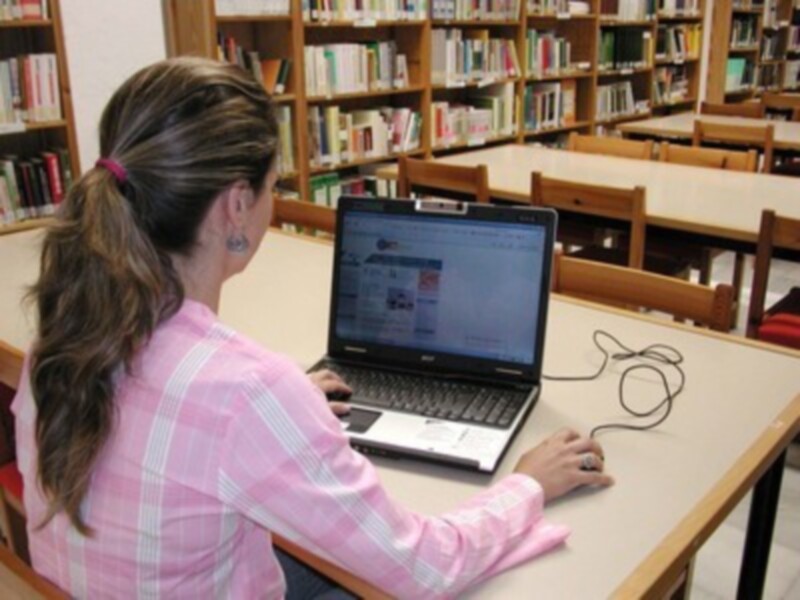 Persona trabajando en un laptop en una biblioteca bien iluminada.