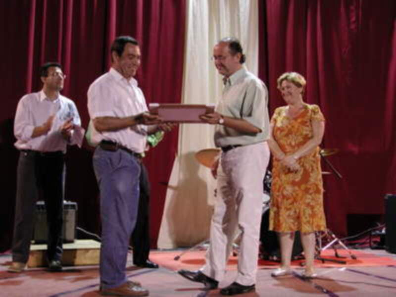 Premio en un evento formal en escenario con cortinas rojas y público observando.