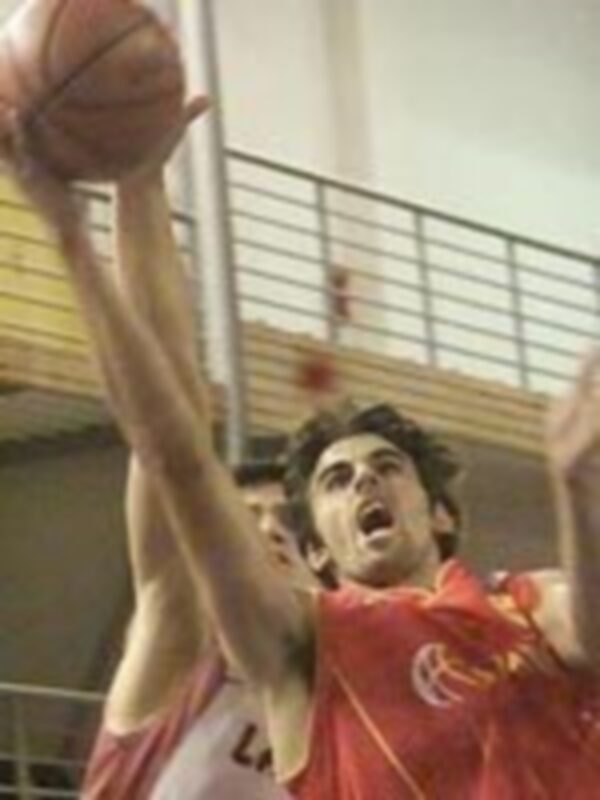 Jugadores de baloncesto en acción durante un partido, uno en rojo y otro en blanco, en un entorno deportivo interior.
