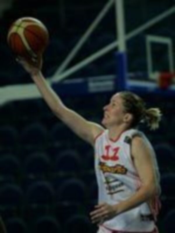 Jugadora de baloncesto en acción durante un partido, lanzando el balón con fuerza.