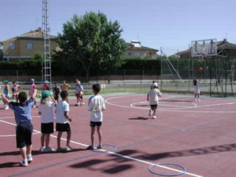 Jóvenes jugando baloncesto en una cancha deportiva al aire libre.