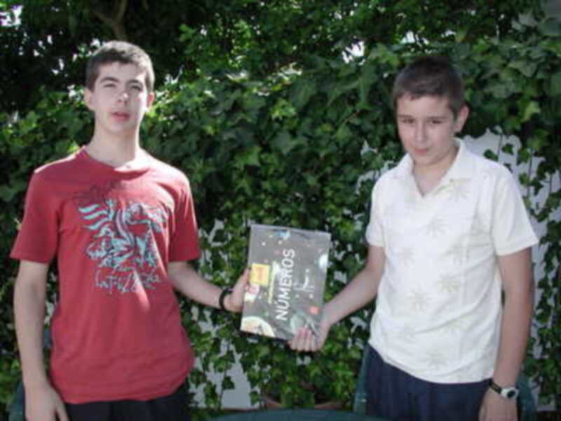 Dos jóvenes posan juntos sosteniendo un libro titulado 'Números' al aire libre.