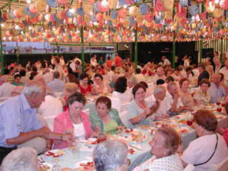 Una reunión social con numerosas personas sentadas en mesas, iluminadas por numerosas lámparas colgantes.