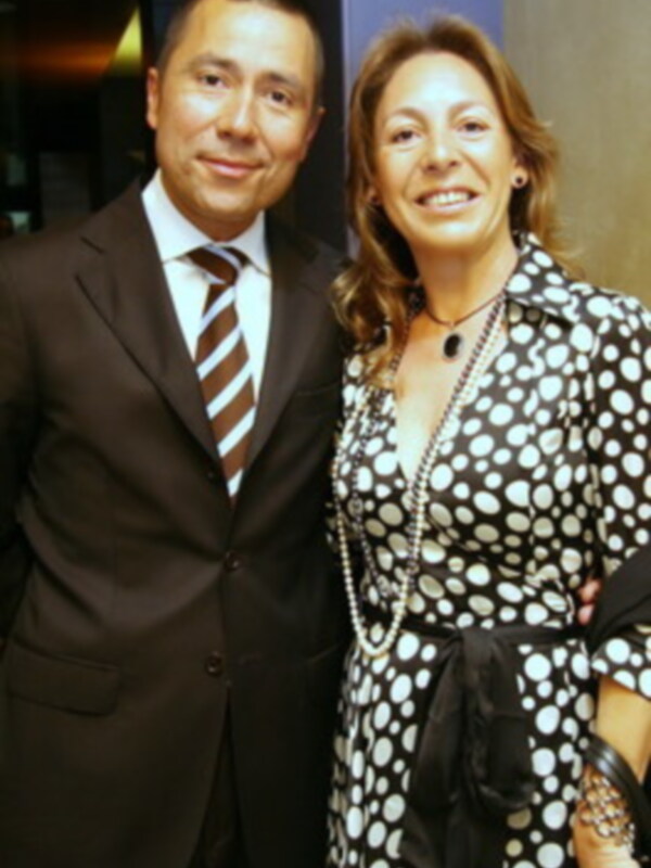Dos personas sonrientes posando juntas, él con traje y corbata, ella con vestido de lunares y collar de perlas.