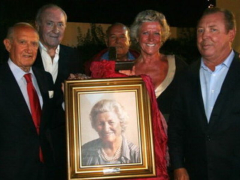 Una foto de grupo de personas posando con un marco que contiene una foto de una anciana sonriente.