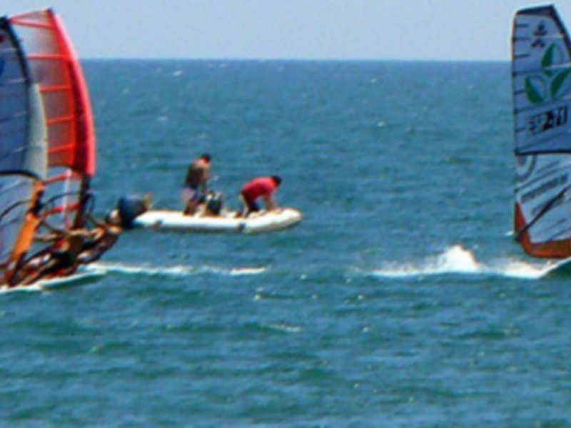 Dos personas practicando windsurf en el mar bajo un cielo azul claro.