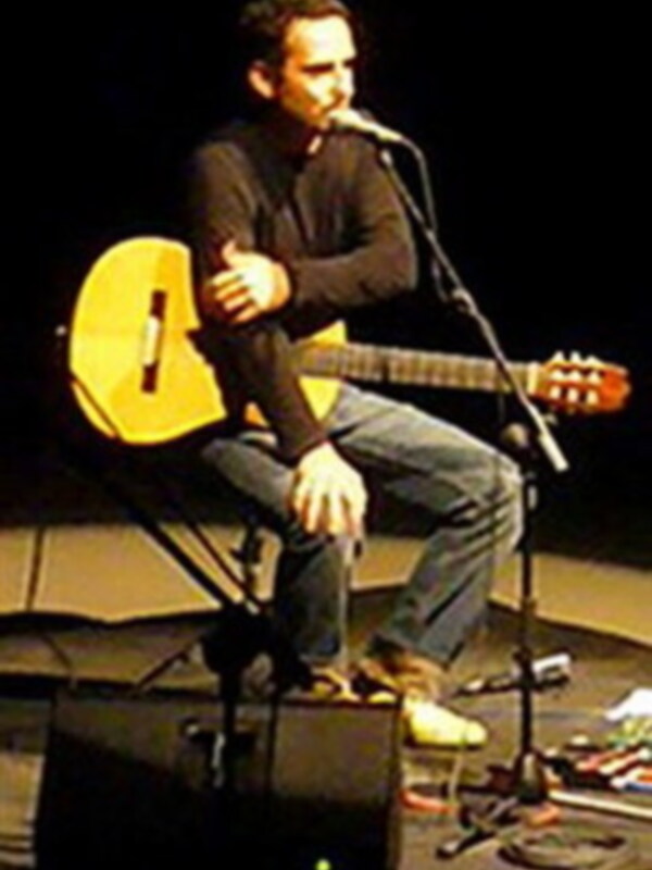 Músico interpretando en un escenario con guitarra acústica y micrófono