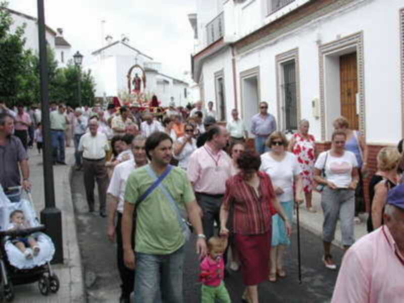 Procesión religiosa en una calle de pueblo, con personas caminando y portando una imagen de la Virgen.