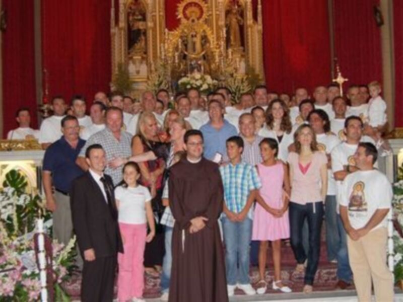 Una imagen de una celebración religiosa en una iglesia, con una persona en traje negro y otros en ropa casual, posando para la foto en el centro de la imagen.