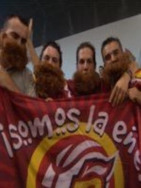 Grupo de personas con barbas y camisetas rojas celebrando con un cartel que dice 'Somos la Leyenda'.