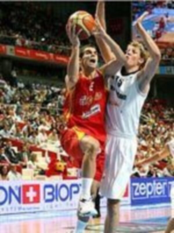 Jugadores de baloncesto en acción durante un partido, uno en rojo y otro en blanco, en un estadio lleno de espectadores.