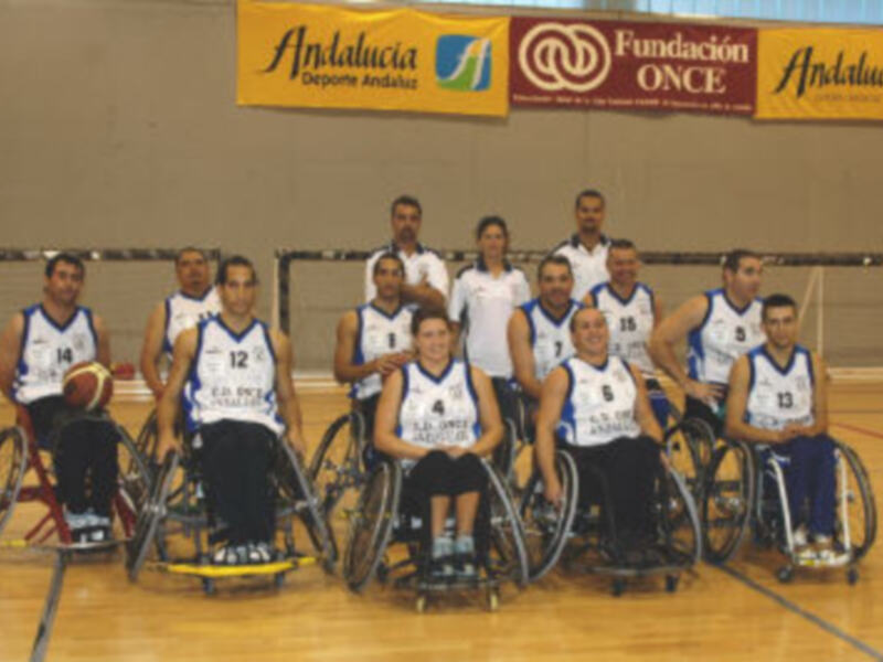 Equipo de baloncesto en silla de ruedas posando para una foto en una cancha deportiva.