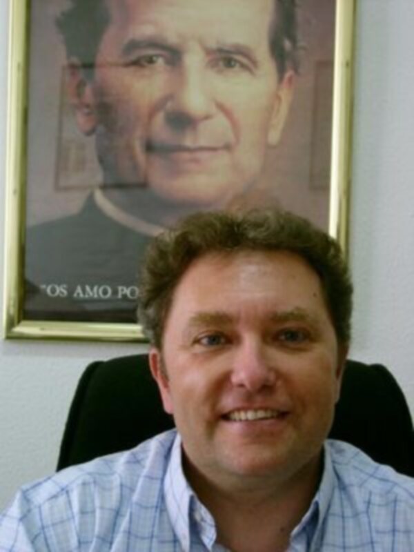 Persona sonriente frente a un retrato enmarcado de un sacerdote.