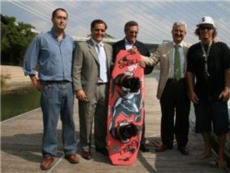 Grupo de hombres posando con un tablero de wakeboard y un barco de remolque en un muelle al aire libre.