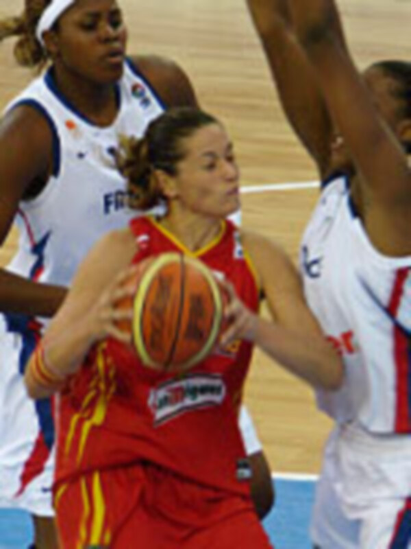 Jugadora en acción durante un partido de baloncesto, vestida con el uniforme de España, controlando el balón bajo la presión de oponentes.