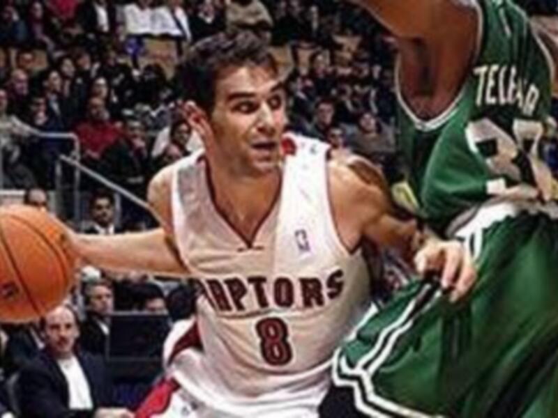 Jugador de los Raptors en acción durante un partido de baloncesto, driblando el balón mientras es marcado por un jugador del equipo rival.