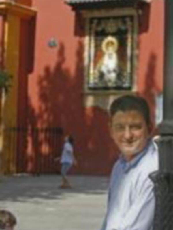 Niño sonriendo en una calle con un mural de la Virgen en el fondo.
