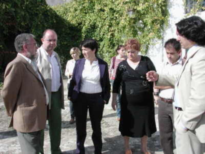 Un grupo de personas conversa en un entorno al aire libre, rodeado de vegetación y edificios históricos.