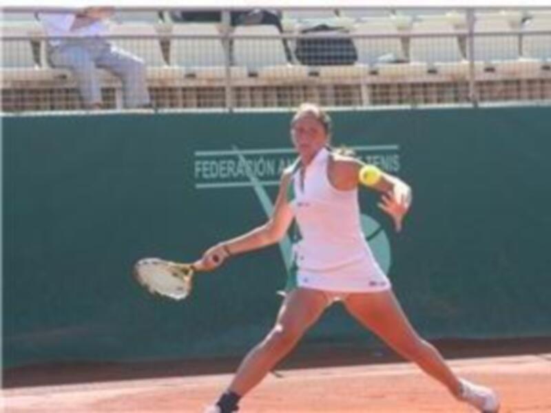 Una jugadora de tenis en acción, con el escudo de la Federación Nacional de Tenis en el fondo.