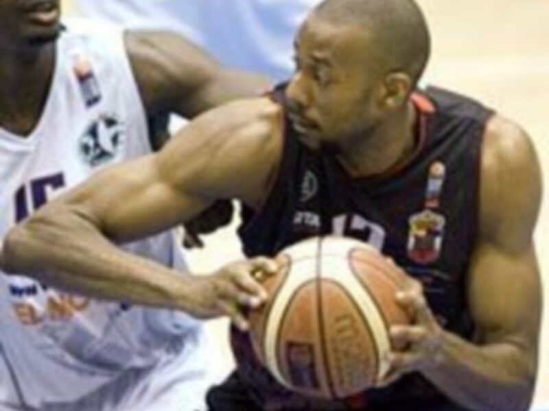 Un jugador de baloncesto en acción, con el número 12 en su camiseta, luchando por controlar el balón mientras un rival lo intenta bloquear.