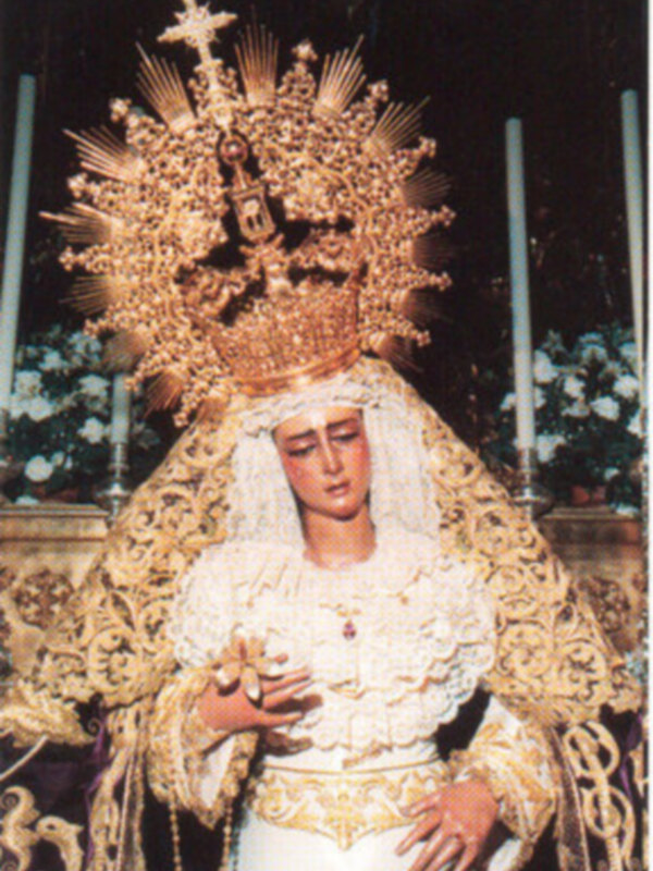 Imagen de la Virgen de la Soledad, vestida con traje blanco y adorno dorado, representando la devoción católica.