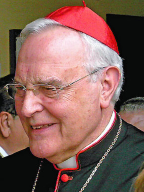 Retrato de un cardenal sonriendo, vistiendo la típica capa roja y collar de la Iglesia Católica.