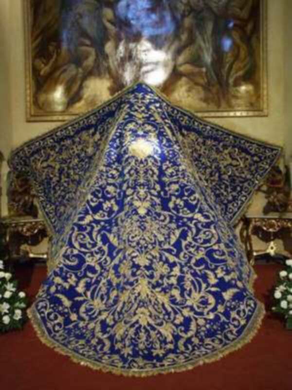 Vestimenta ceremonial azul con bordados dorados, colgando en un entorno religioso con pinturas al fondo.